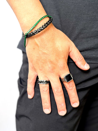Pulseira masculina em aço inox black com zircônias verdes da UNA Semijoias e Aço no pulso em close, combinada a anéis escuros, em fundo claro e look casual.