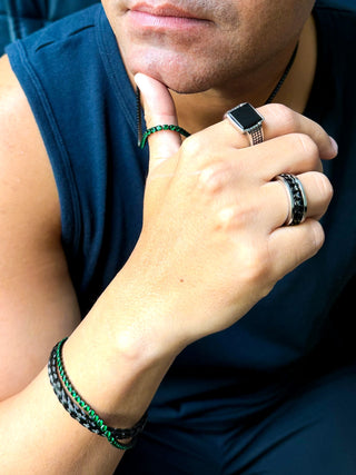 Pulseira masculina em aço inox black com detalhes verdes no pulso, com anéis em aço e colar combinando, em foto de lifestyle UNA Semijoias e Aço.