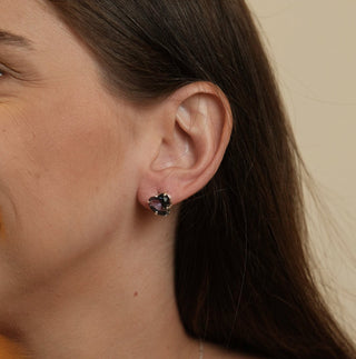 Brinco pequeno de coração com pedra de vidro azul escuro banhado a prata 925 da UNA Semijoias e Aço em fundo branco, em vista frontal do par.