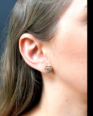 Brinco coração cravejado banhado a ouro 18k da UNA Semijoias e Aço na orelha feminina em close lateral, com pedra em forma de coração em destaque.