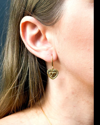 Brinco coração Espírito Santo folheado a ouro 18k da UNA Semijoias e Aço na orelha feminina em close lateral, com detalhes em relevo dourado.