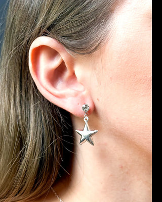 Brinco estrela banhado a prata 925 da UNA Semijoias e Aço na orelha feminina em close lateral, com pingente de estrela lisa pendente