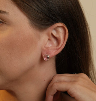 Brinco pequeno de coração com pedra de vidro rosa claro banhado a prata 925 da UNA Semijoias e Aço em fundo branco, em vista frontal do par.