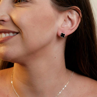 Modelo usando brinco pequeno trevo preto banhado a prata 925 da UNA Semijoias & Aço, close na orelha com luz natural e fundo neutro.