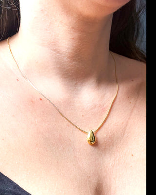 Colar delicado com pingente em formato de gota banhado a ouro 18k da UNA Semijoias e Aço no colo feminino, em fundo neutro, com corrente fina em destaque.