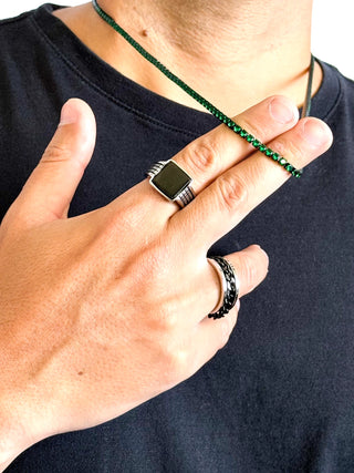 Colar masculino em aço inox black com pedras verde-esmeralda da UNA Semijoias e Aço em close na mão do modelo, mostrando brilho e acabamento fino.