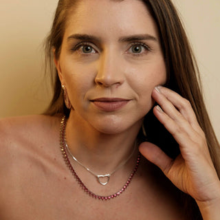 Colar riviera 3 pontas rubi banhado a ouro 18K da UNA Semijoias e Aço no colo feminino em close, com camada dupla de colares em destaque.