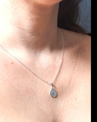 Colar São Bento banhado a prata 925 da UNA Semijoias e Aço no colo feminino em close, com medalha religiosa delicada em destaque.