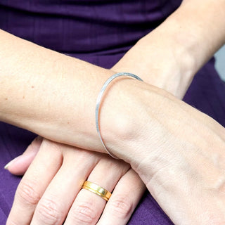 Pulseira fita banhada a prata minimalista no pulso feminino, UNA Semijoias e Aço, em look com vestido roxo.