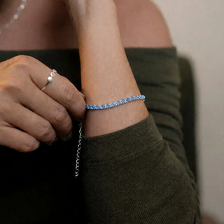 Pulseira riviera azul claro banhada a prata 925 da UNA Semijoias e Aço no pulso feminino em close, com pedras azul-claro e corrente ajustável em destaque.