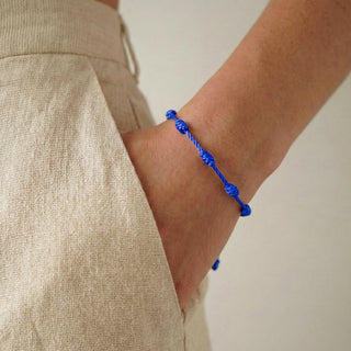 Pulseira verão nozinho da sorte azul da UNA Semijoias e Aço no pulso feminino, em close lateral, combinada com look casual em tecido claro.