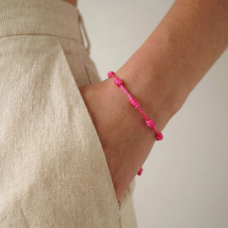Pulseira verão nozinho da sorte rosa da UNA Semijoias e Aço no pulso feminino, em close lateral, combinada com look claro e casual de verão.