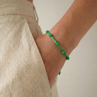 Pulseira verão nozinho da sorte verde da UNA Semijoias e Aço no pulso feminino, em close lateral, combinada com look claro e casual de verão.